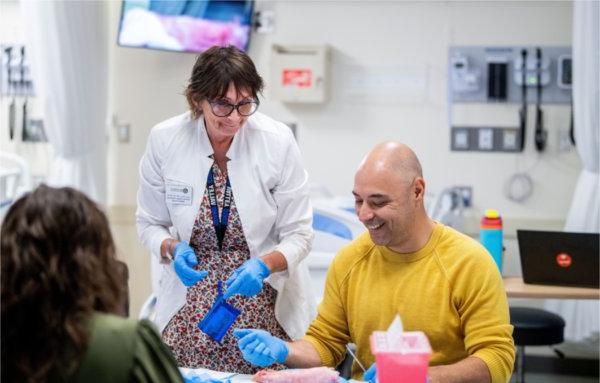 亨利·佩纳 seated laughs with a professor in a white coat during a suturing lab