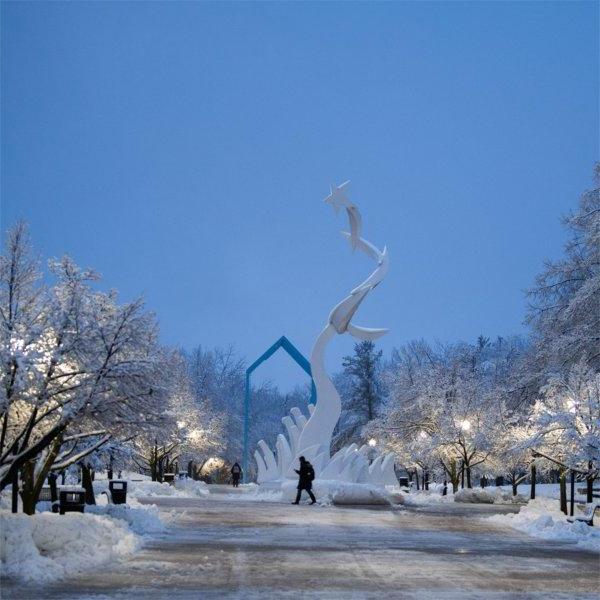 黎明时分，一个人走过下雪的大学校园里的一座雕塑.