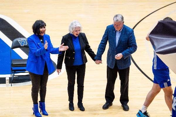  A university president wearing blue claps as a basketball court named after a former university president, 图为他与妻子手牵手, 是公布. 