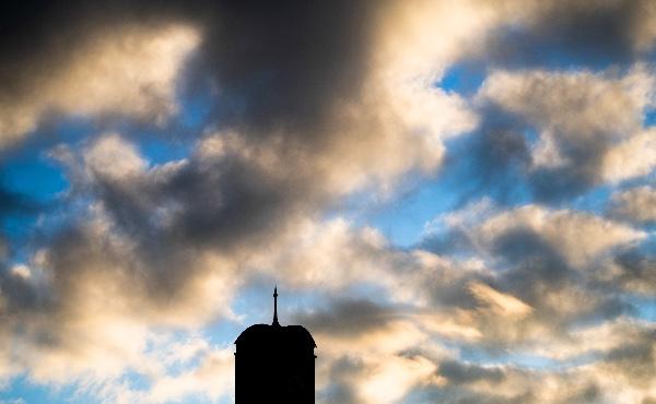  A carillon tower is silhouetted against a cloudy blue and golden sunrise.