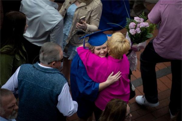  一名毕业生被一名手持粉色鲜花的人拥抱. 